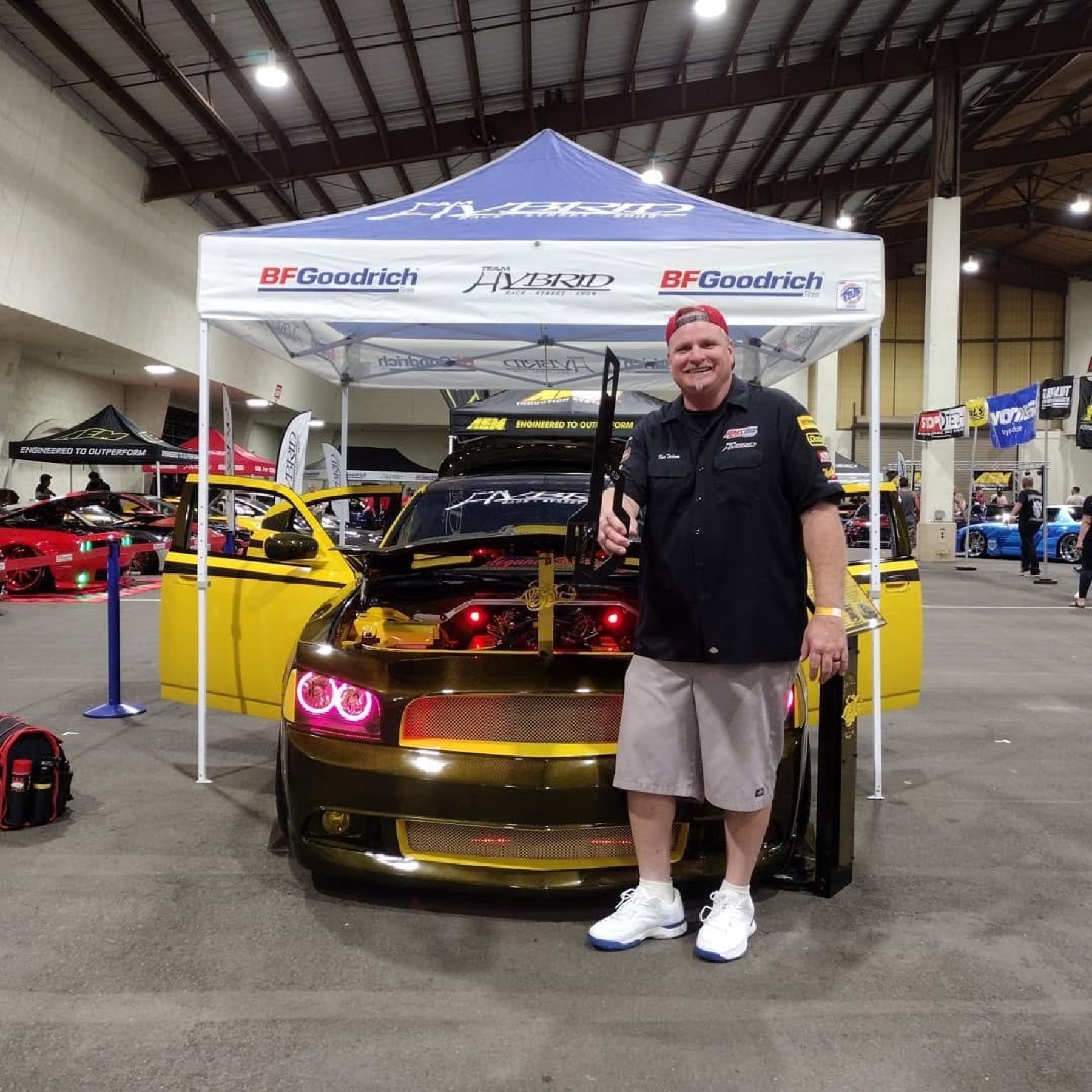 Ken holding a trophy in front of the Super Bee at the Team Hybrid tent